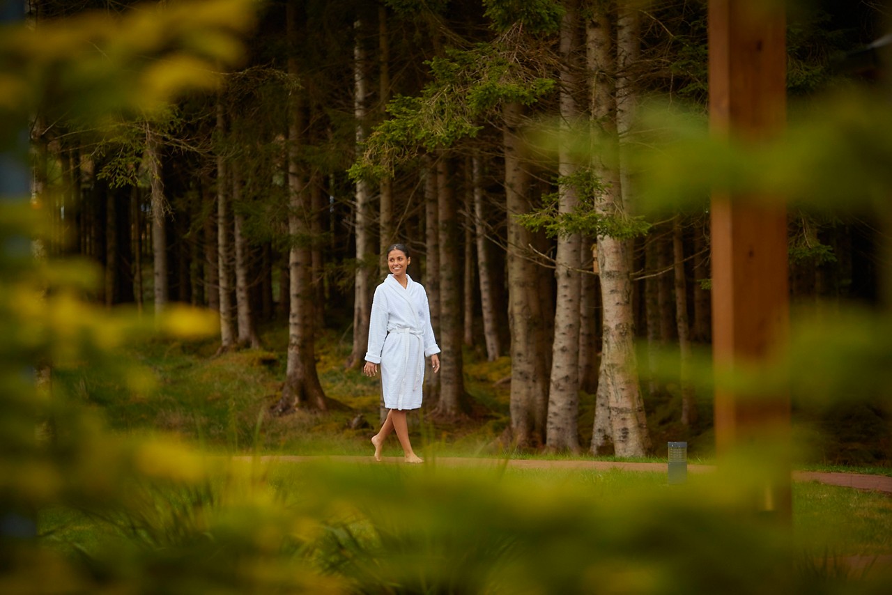 Lady dressed in a soft spa robe as she walks bare foot along a forest path.